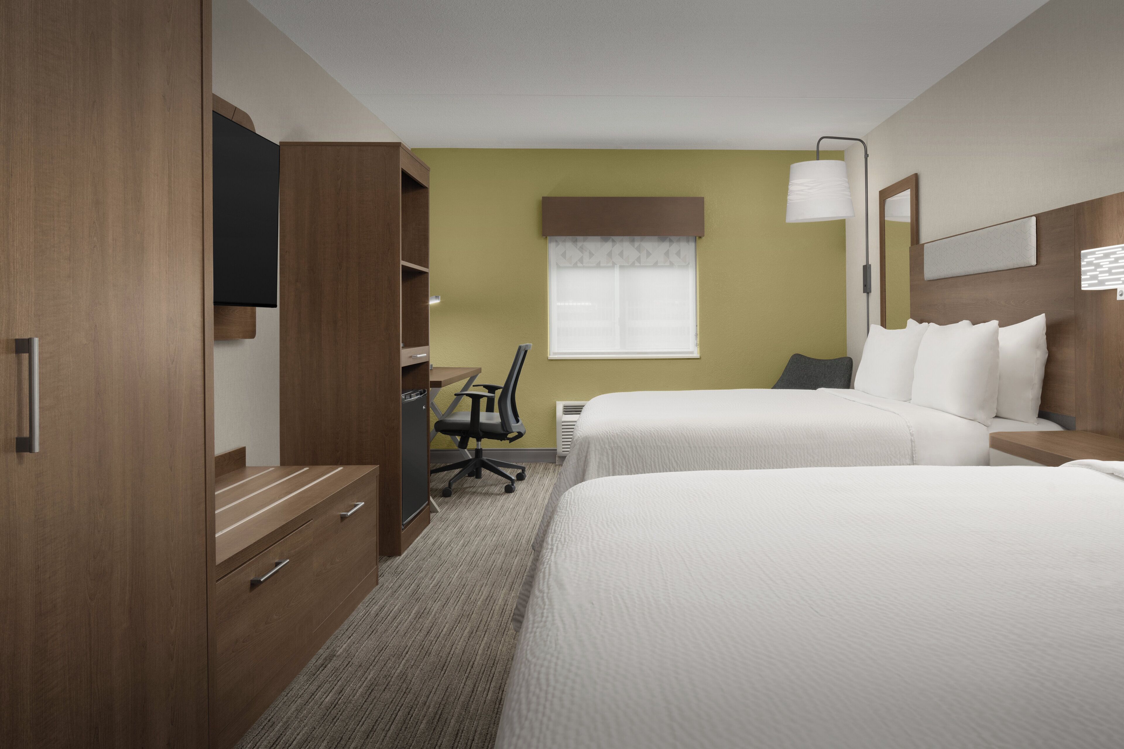 Ein Hotelzimmer mit zwei Betten, einem Schreibtisch mit Stuhl, einem Fernseher und einem Fenster mit Vorhängen.