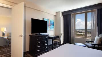 Habitación de hotel con cama, escritorio, silla, televisor y un amplio ventanal con vistas.