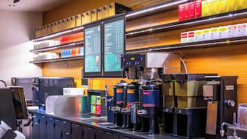 Mostrador de cafetería con varias máquinas de café, un tablero de menú y estantes con productos de café.