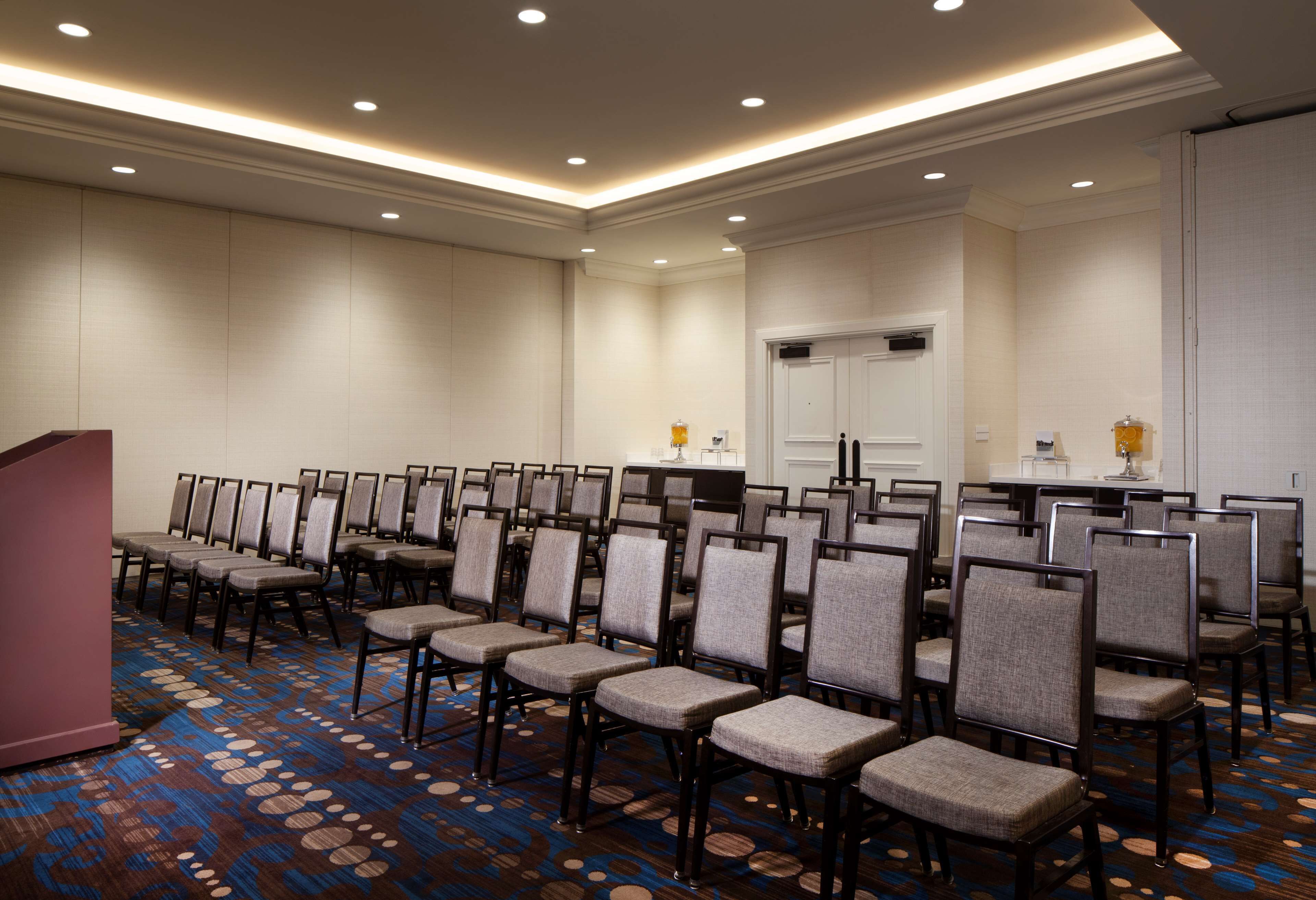 A conference room with rows of chairs, a podium, and a carpeted floor.