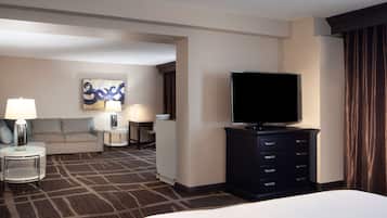 A hotel room with a large bed, a flat-screen TV, a sofa, two side tables with lamps, and a wall art piece.