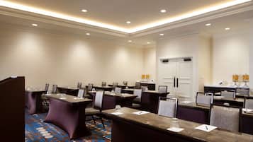 A conference room with multiple tables and chairs, a patterned carpet, and a white door in the background.