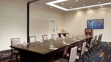Un salón de conferencias con una larga mesa, sillas, un atril y un cuadro en la pared.