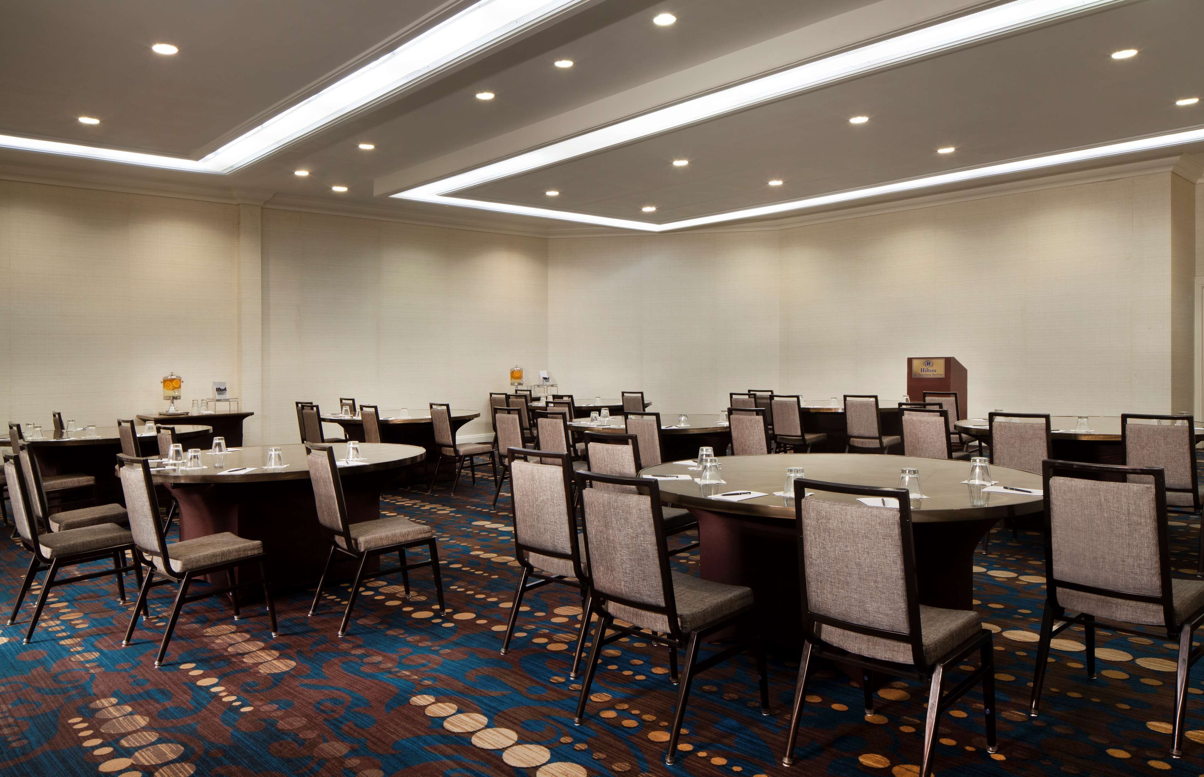 A conference room with multiple tables and chairs, a carpeted floor, and a modern ceiling design.