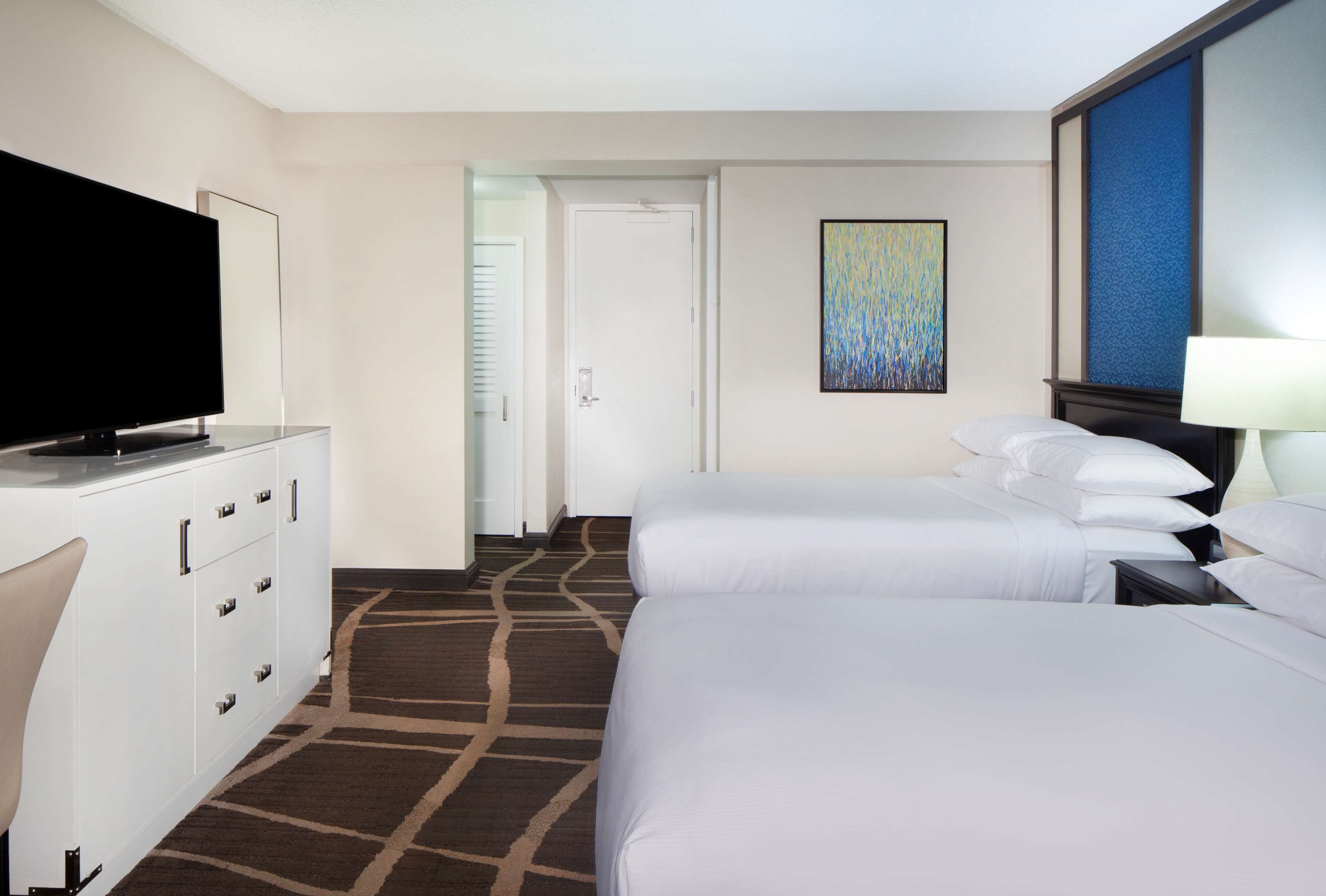 Une chambre d’hôtel avec deux lits, un téléviseur posé sur une commode, une porte et un tableau accroché au mur.