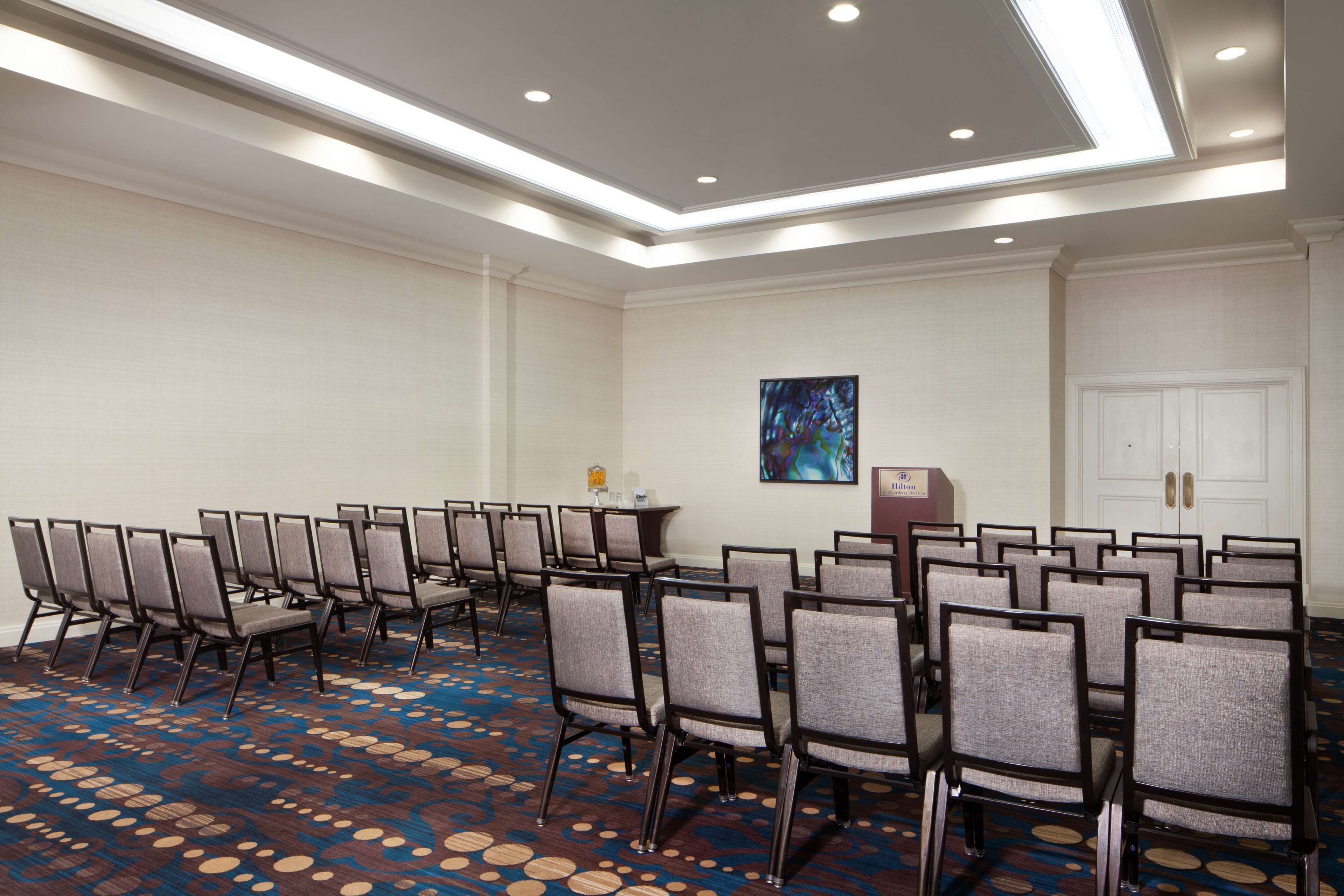 Une salle de conférence avec des rangées de chaises, un pupitre et une porte.