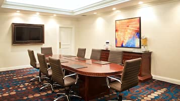 Una sala de conferencias con una gran mesa ovalada, seis sillas, un televisor de pantalla plana, un cuadro decorativo y una nevera pequeña.