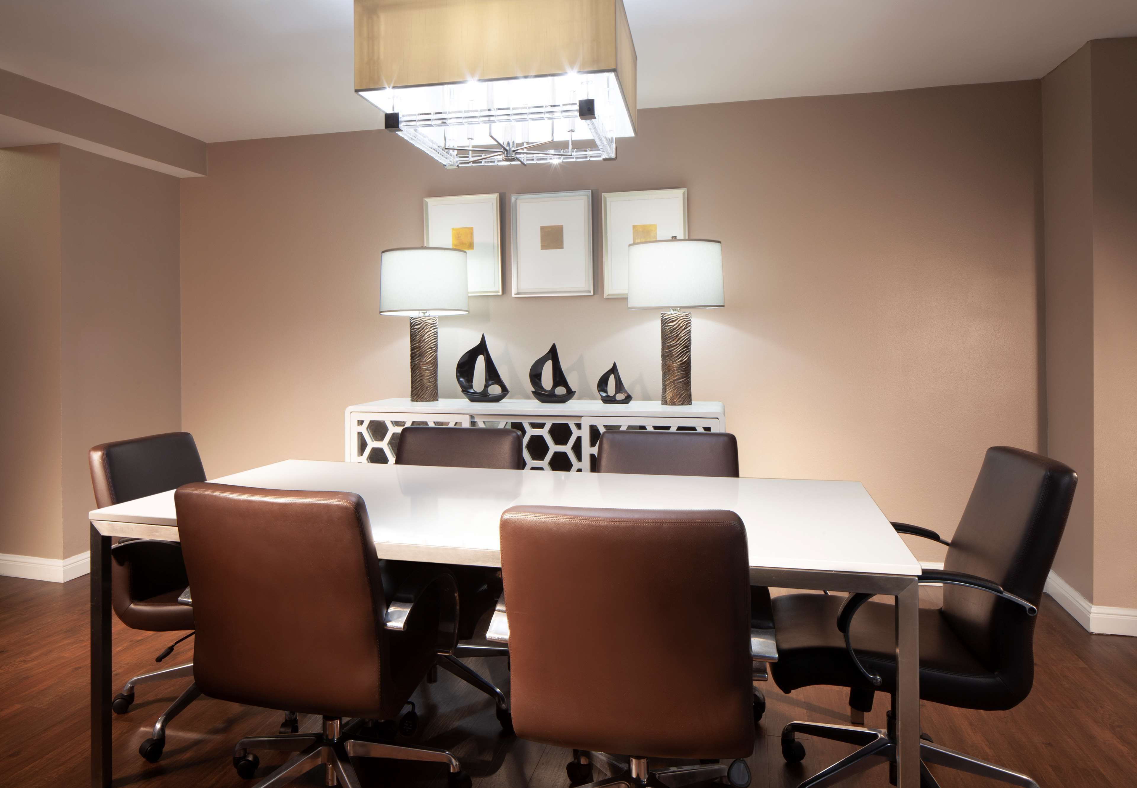 A conference room with a long table, four chairs, and three wall-mounted lamps.