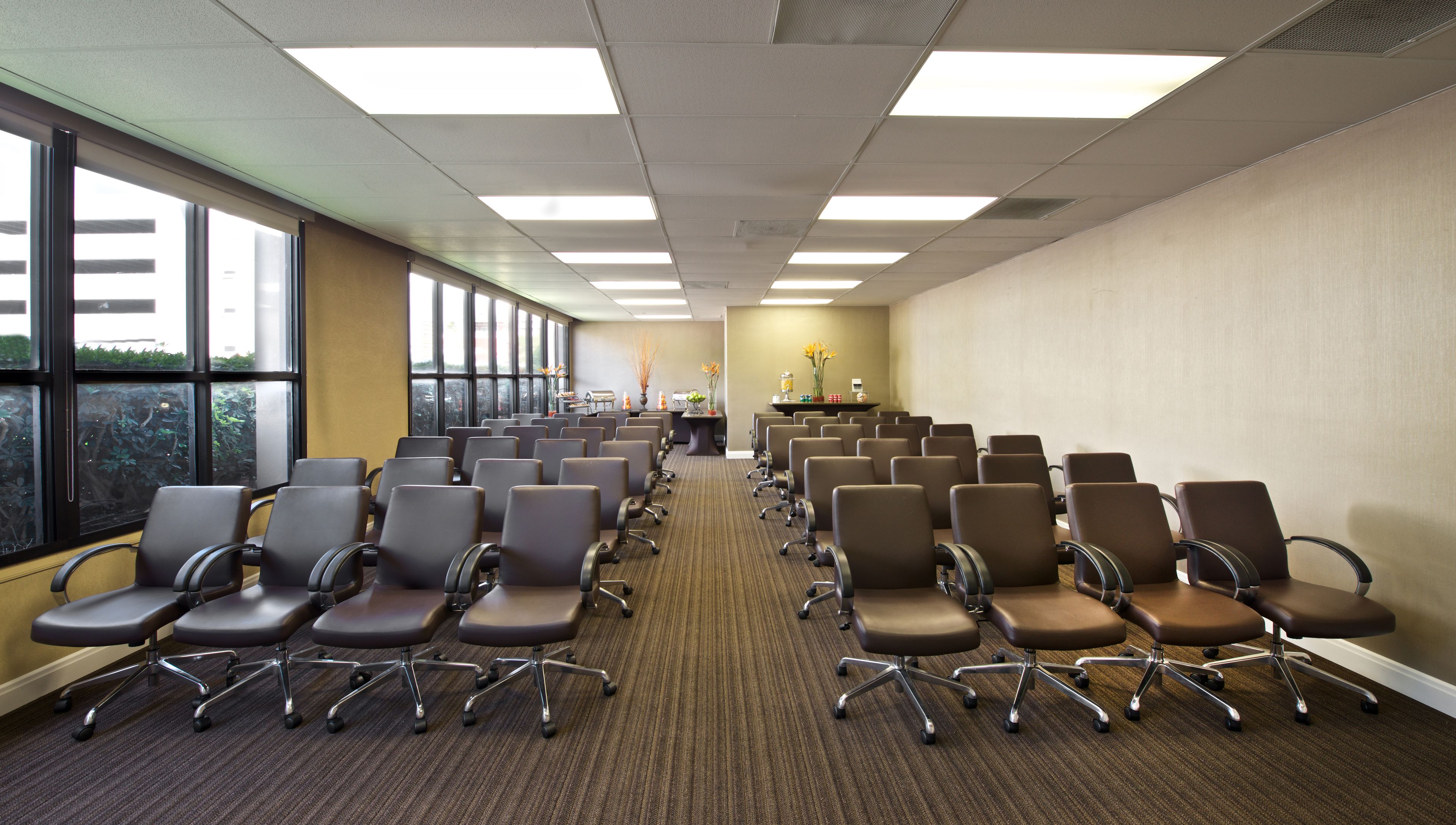 A conference room with rows of chairs, a carpeted floor, and large windows on one side.