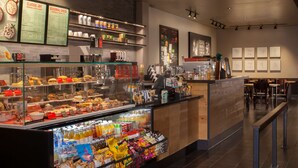A coffee shop interior with a display case of pastries, a refrigerated section with juices and snacks, and a menu board above the counter.