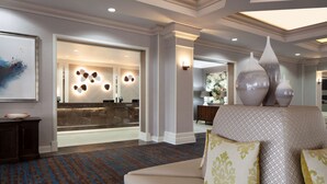 Een hotellobby met een receptiebalie, een kamerbreed tapijt met dessin en een bank met decoratieve kussens.