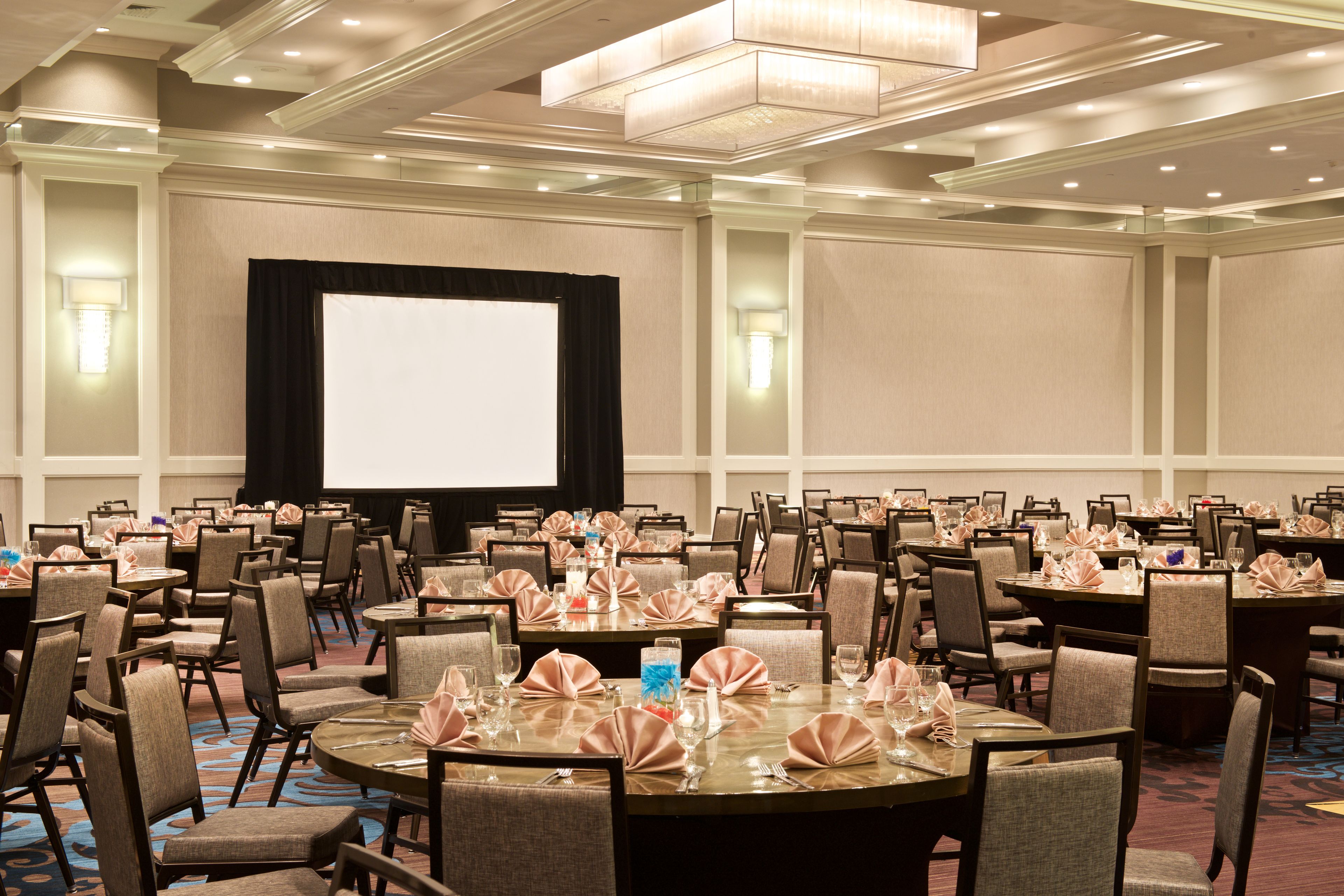 A conference room with multiple round tables, chairs, and a large screen for presentations.