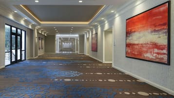 A hotel corridor with patterned carpet, framed artwork, and recessed lighting.