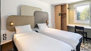 Habitación de hotel con dos camas, un armario, un escritorio y una ventana con vista a árboles.