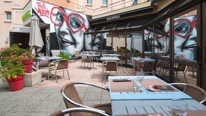 Un área de café al aire libre con mesas y sillas, un mural en la pared y un cartel de B&B Hotels.