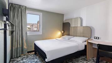 Camera d'albergo con un letto, una scrivania, una sedia, una finestra con tende e una lampada a parete.