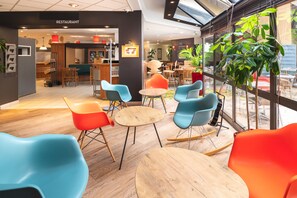 A modern cafe with colorful chairs, wooden tables, and large windows.