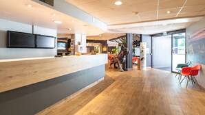 Una zona de recepción moderna con un mostrador de madera, un televisor de pantalla plana y un restaurante al fondo.