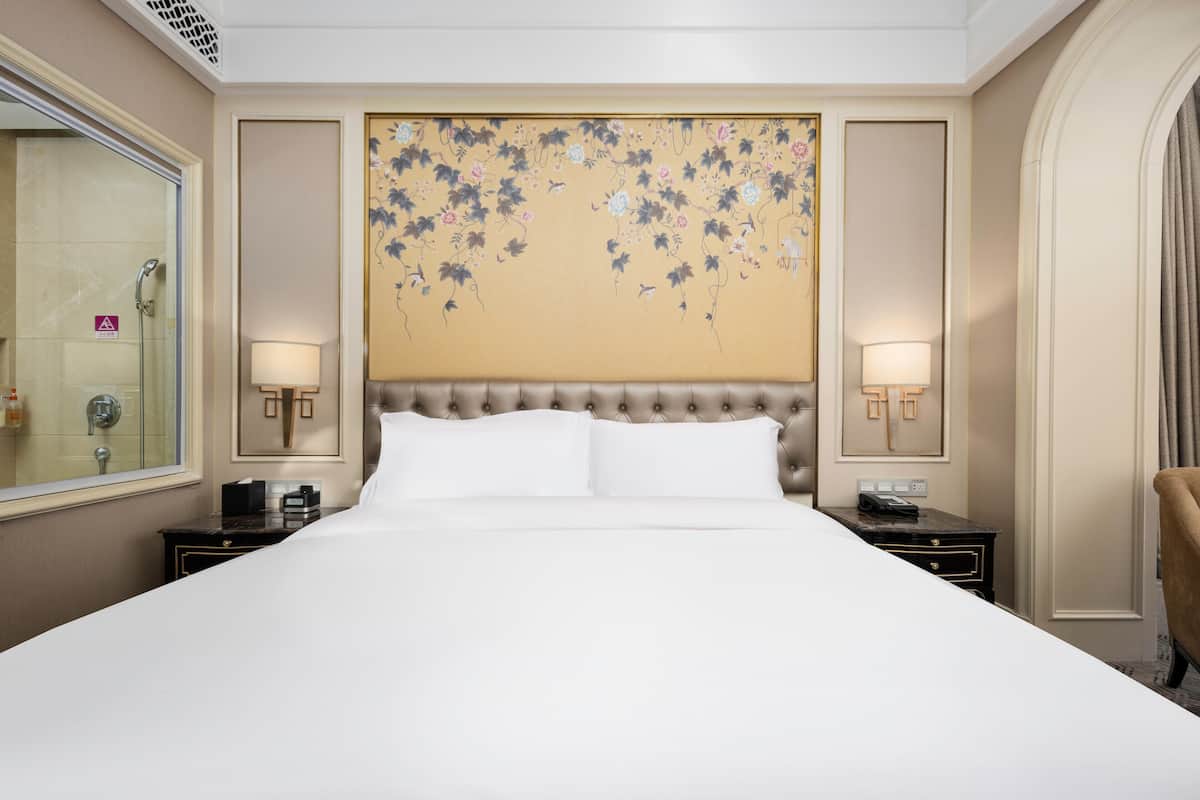 Une chambre d’hôtel avec un grand lit, deux tables de chevet, une tête de lit ornée de motifs floraux et un grand miroir.