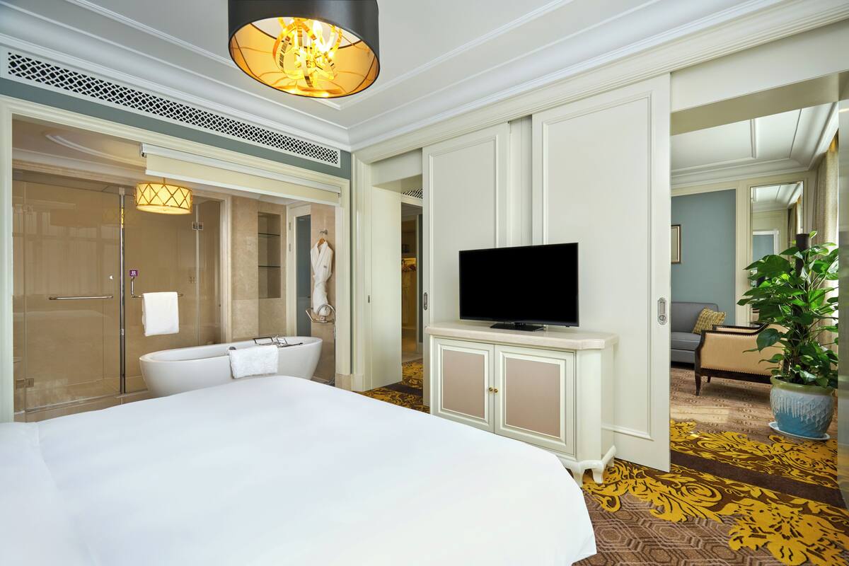 Une chambre d’hôtel avec un grand lit, une télévision, une salle de bain avec baignoire et une plante en pot.