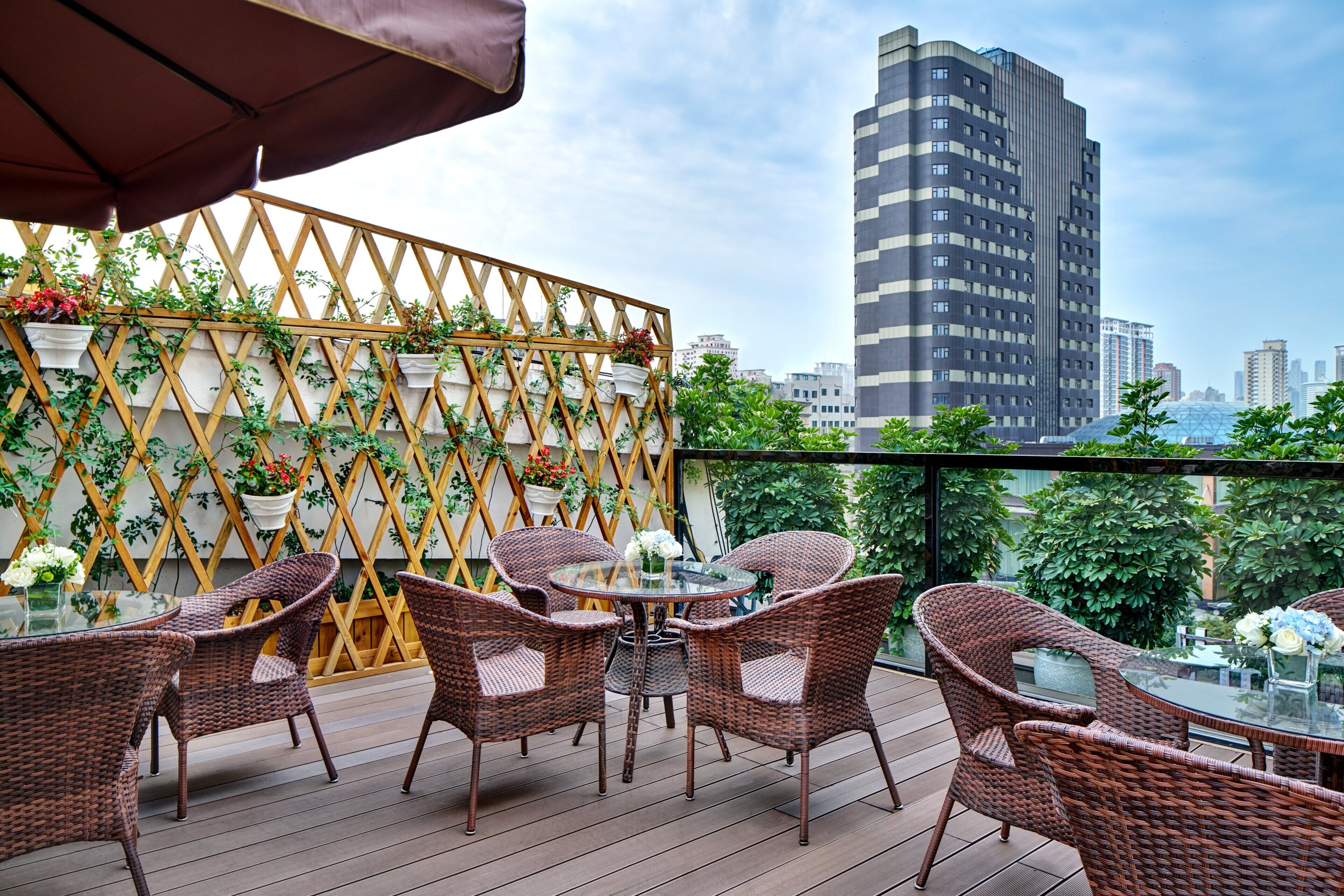 A balcony with wicker furniture and potted plants, overlooking a cityscape with modern buildings.