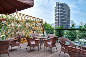 Un balcon agrémenté de meubles en osier et de plantes en pot, offrant une vue sur un paysage urbain avec des bâtiments modernes.