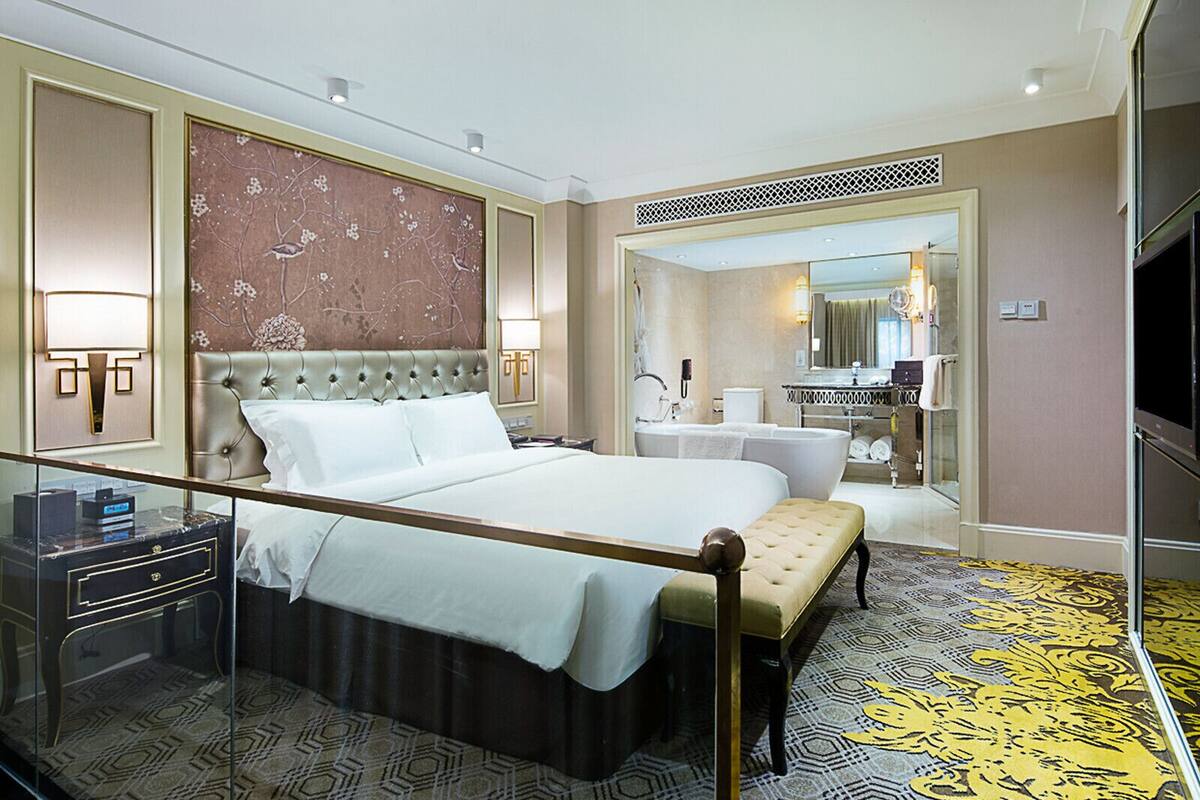 Une chambre d’hôtel avec un grand lit, une table de chevet, un miroir et une salle de bain visible à travers une porte ouverte.