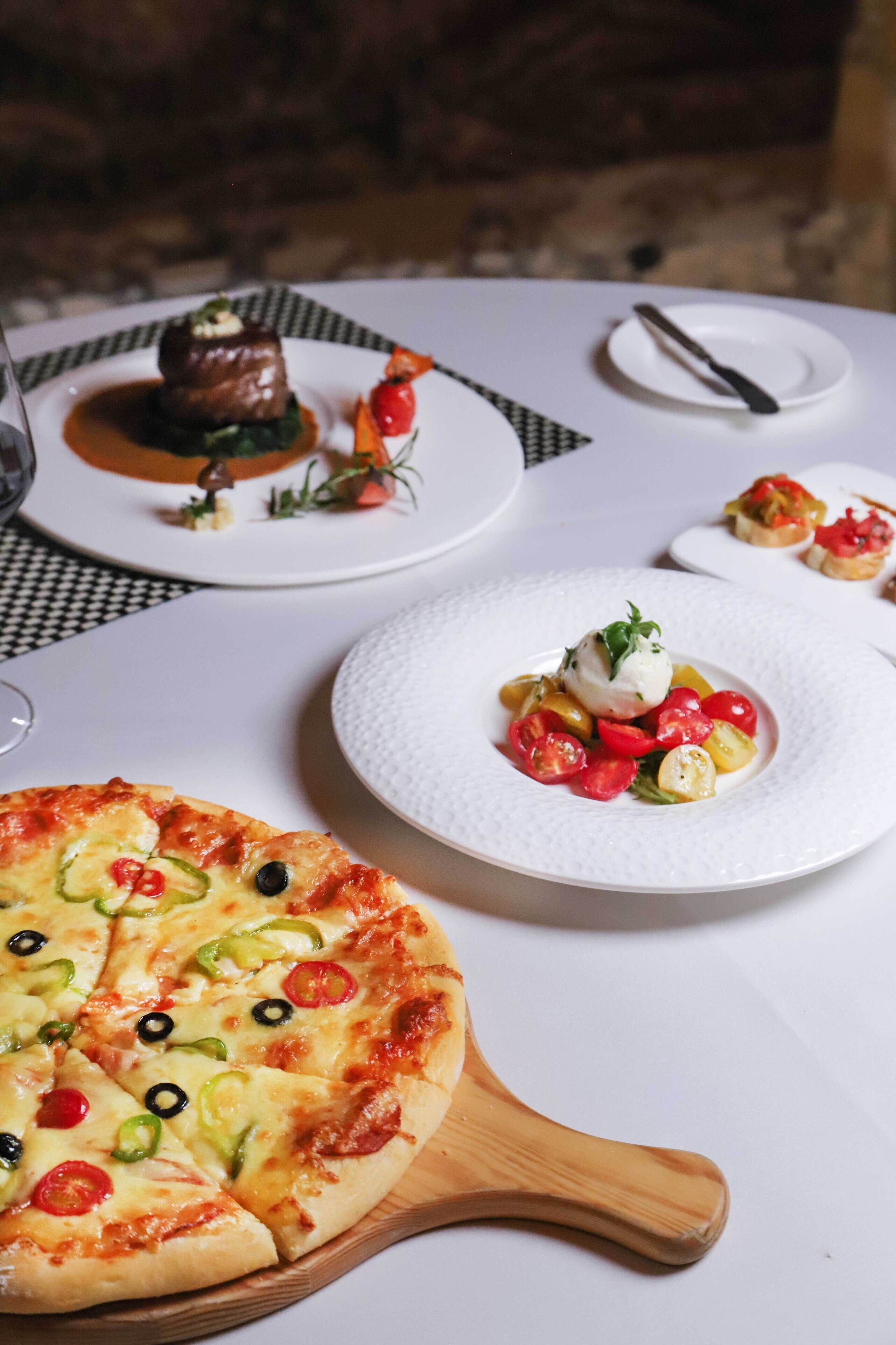 A dining table with a pizza, a plate with a salad, and a dessert.
