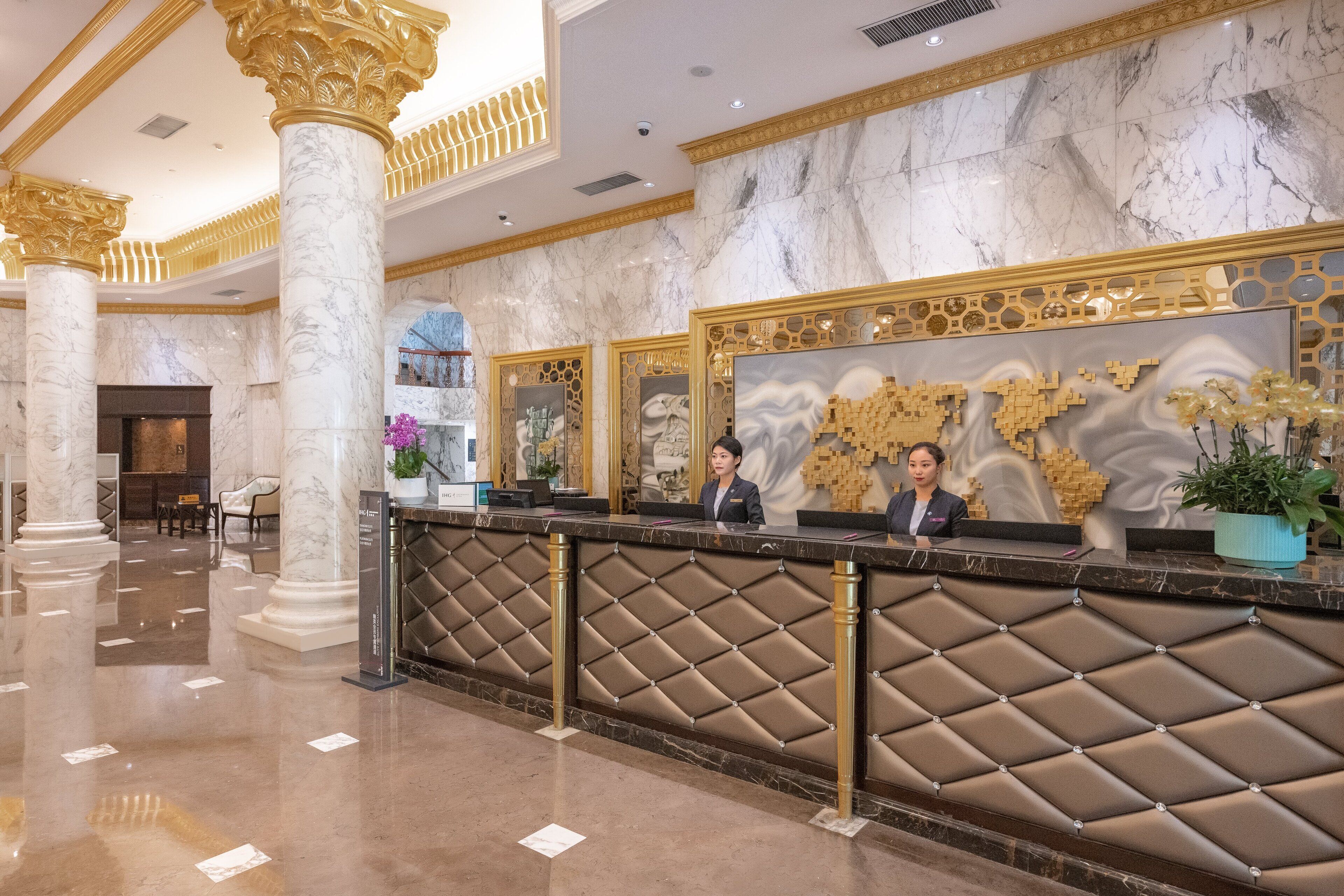 A hotel reception area with marble columns, a reception desk with a patterned design, and a decorative wall.