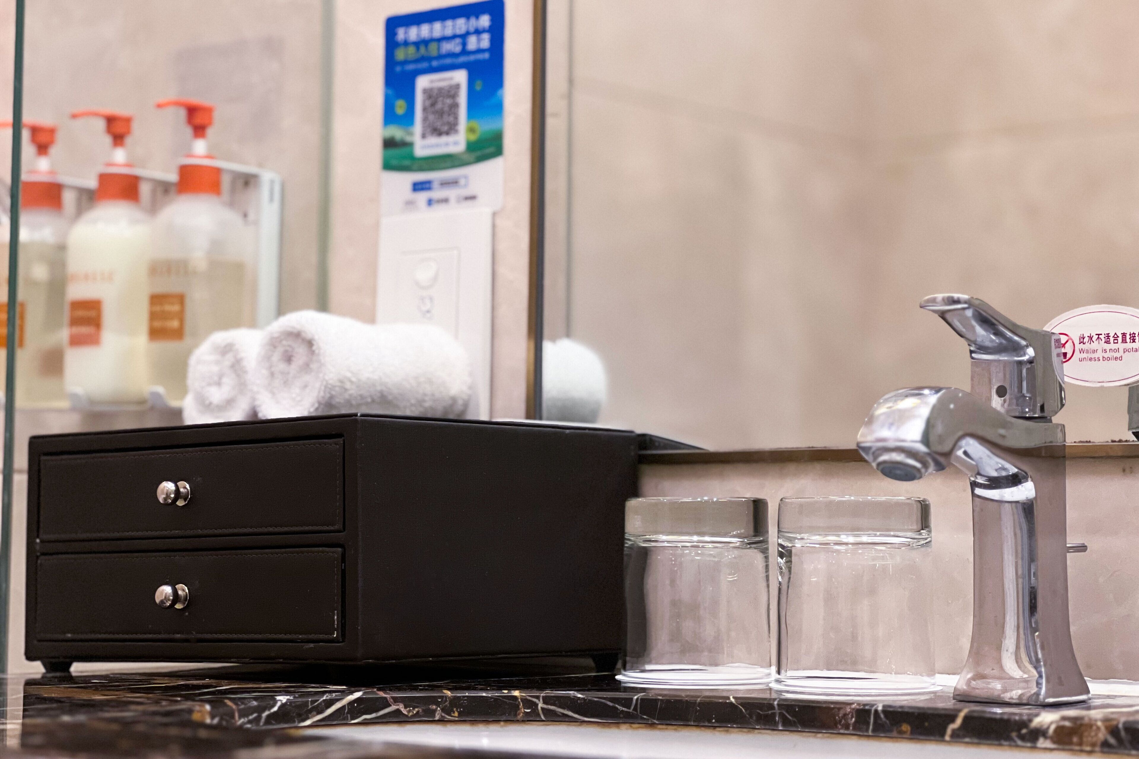 A bathroom with a black vanity, a mirror, a faucet, and two glass tumblers.