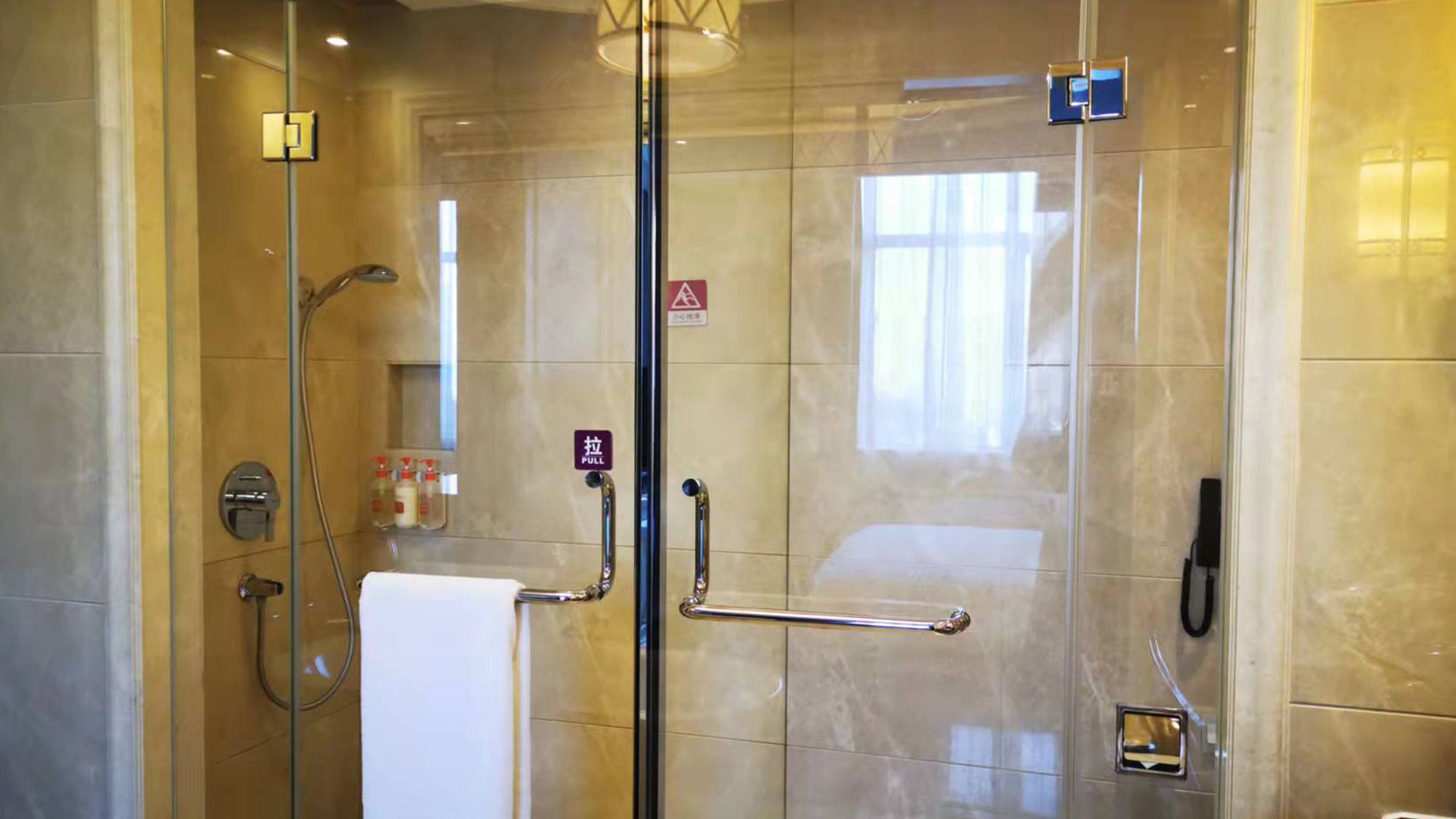 Cabina de ducha con paredes de vidrio, barra de apoyo, perchero y puerta de vidrio con manija.