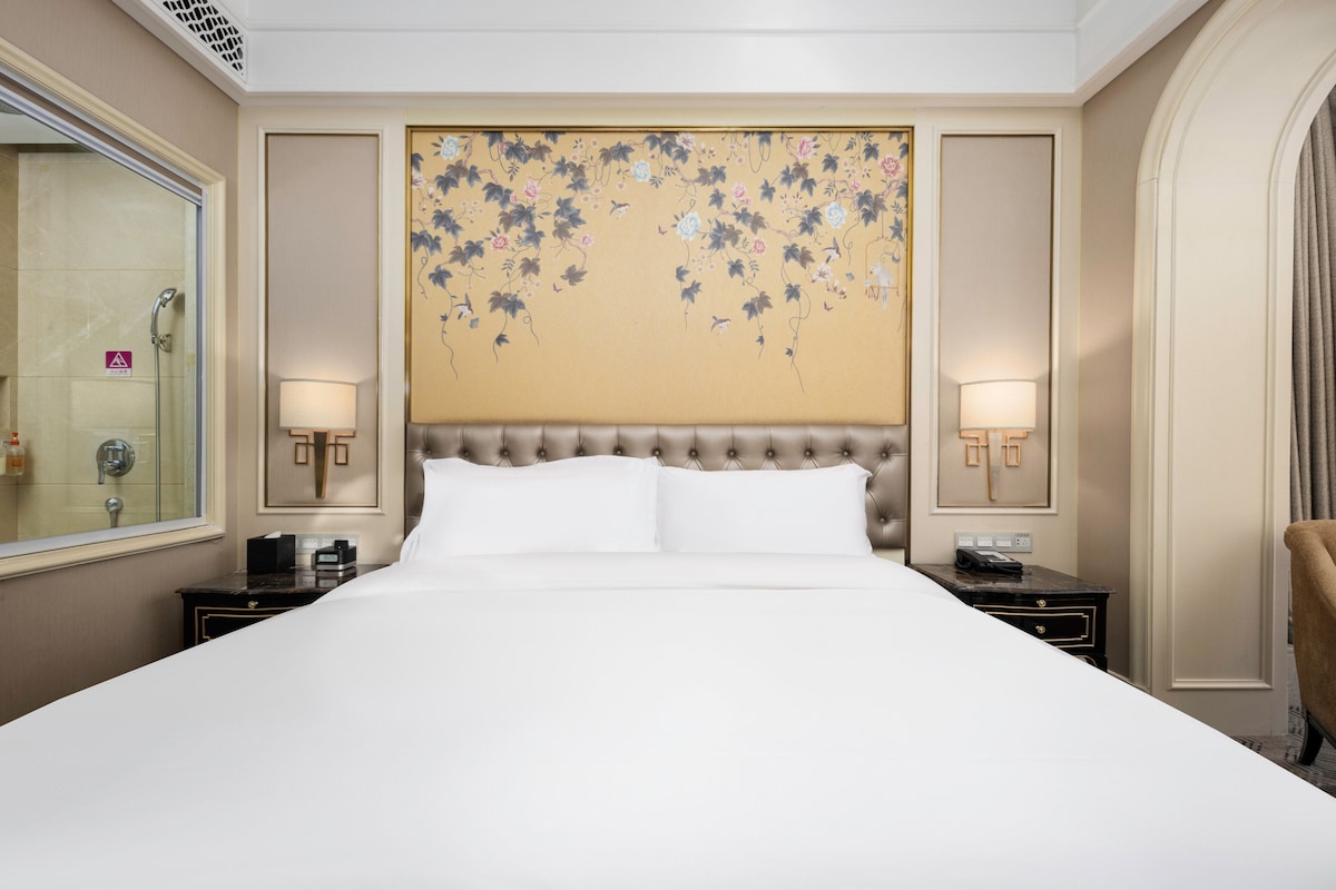 Ein Hotelzimmer mit einem großen Bett, zwei Nachttischen, einem Kopfteil mit floralem Dekor und einem großen Spiegel.