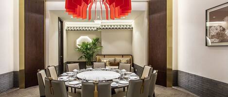 A dining room with a round table set for six, surrounded by upholstered chairs.