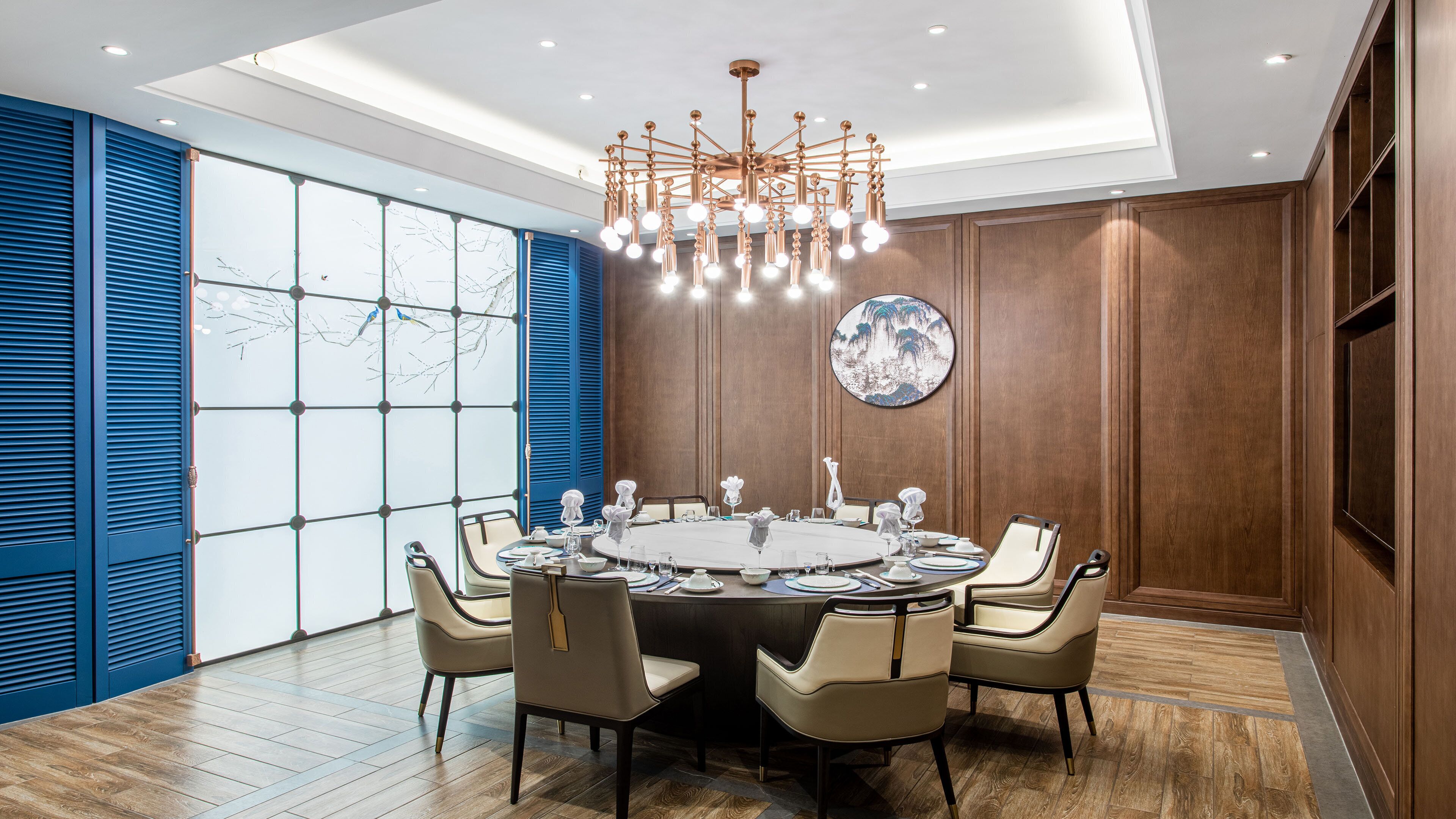 Uma sala de conferências com uma mesa redonda, cadeiras, um candelabro e uma grande janela com persianas.