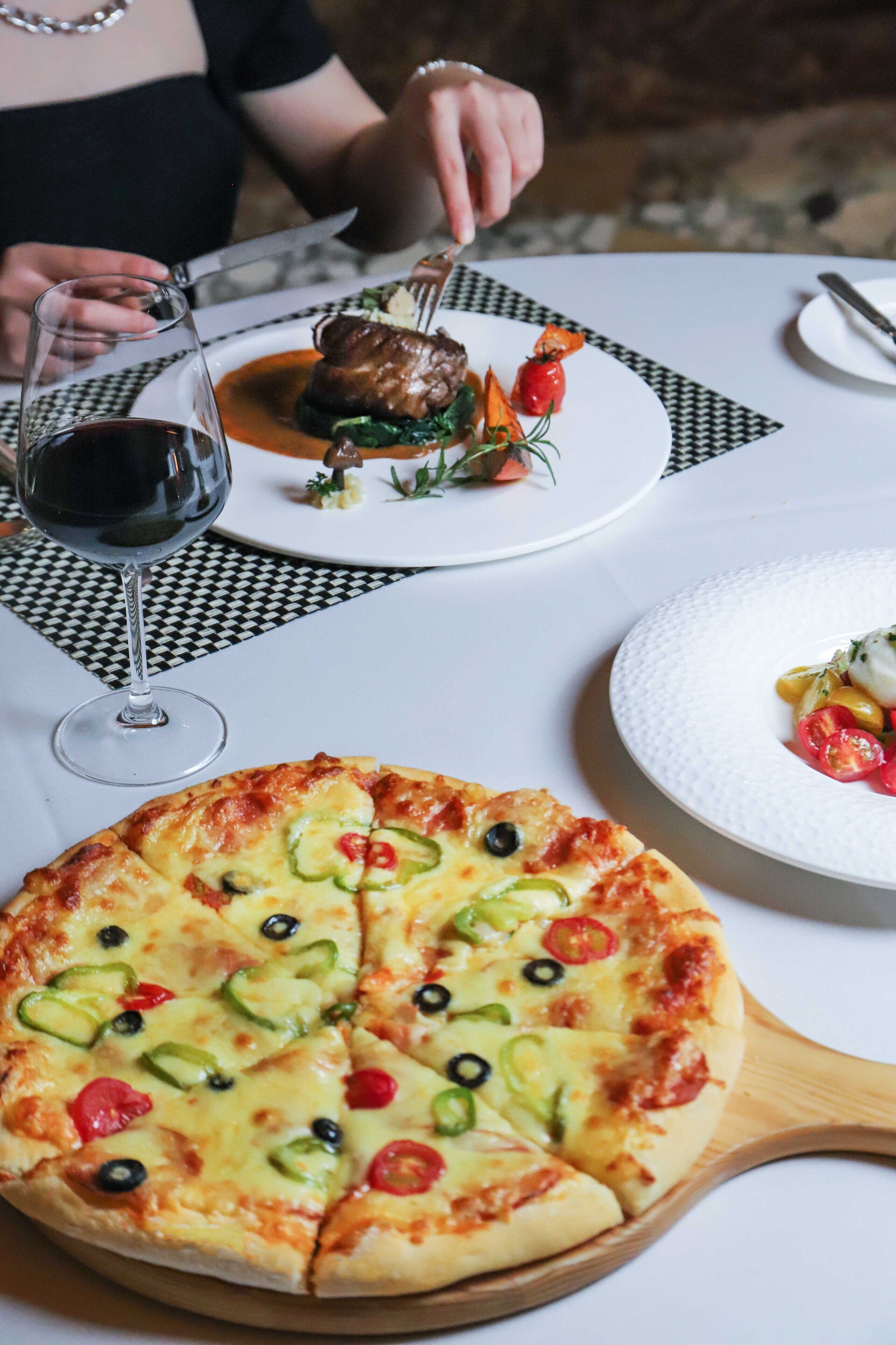 Una mesa con pizza, una copa de vino y un plato de comida.