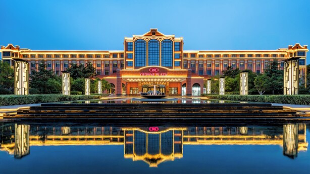 A large, modern hotel with a central fountain and a clear reflection in the water. - Crowne Plaza Zhengzhou by IHG (Zhengzhou)