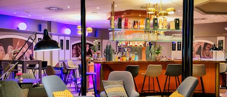 Zona de bar con diversas opciones de asientos, una barra y una variedad de botellas y vasos en estanterías.