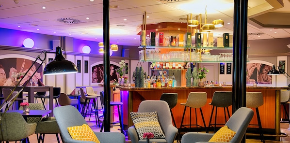 Ett område med bar, där det finns flera olika typer av sittplatser, en bardisk och ett stort utbud av flaskor och glas som står på hyllor.