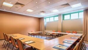 Une salle de conférence avec de longues tables, des chaises et une grande fenêtre avec des rideaux.