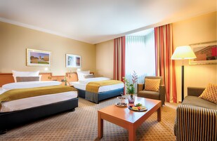 A hotel room with two beds, a sofa, a table with fruit, and a lamp.