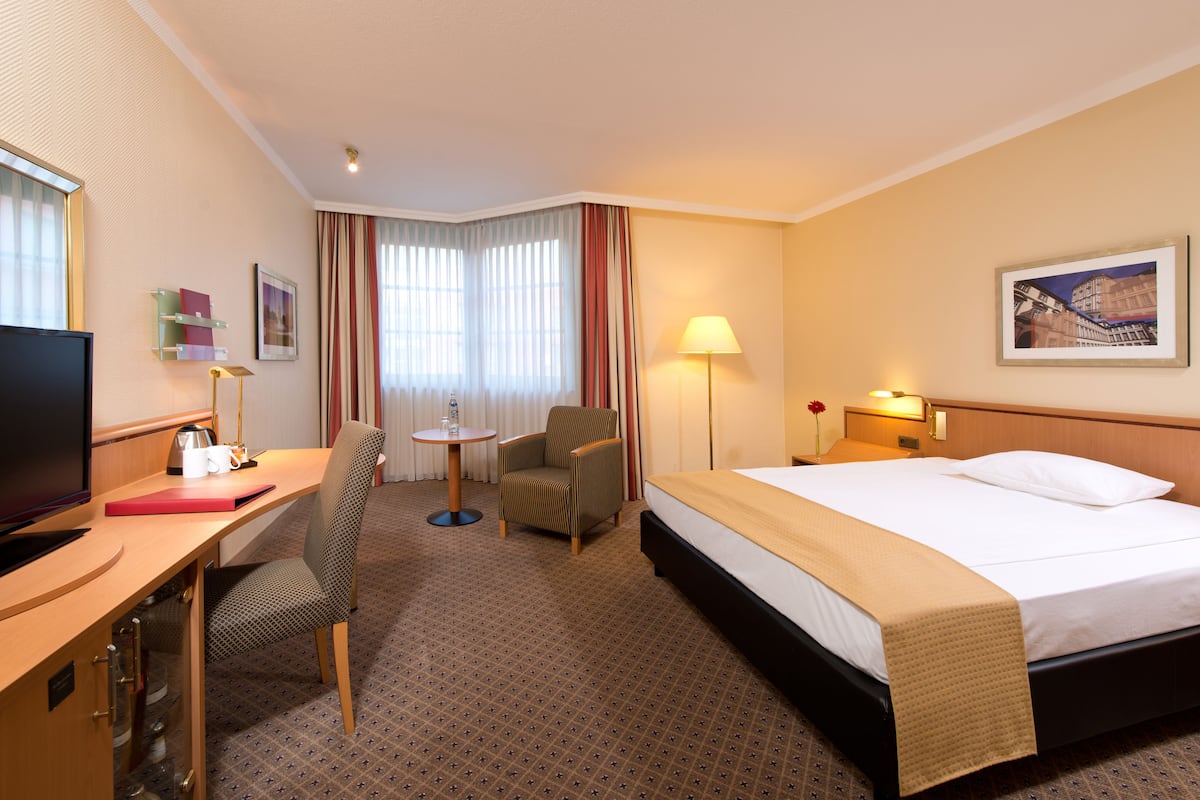 A hotel room with a bed, desk, chair, television, and a lamp.