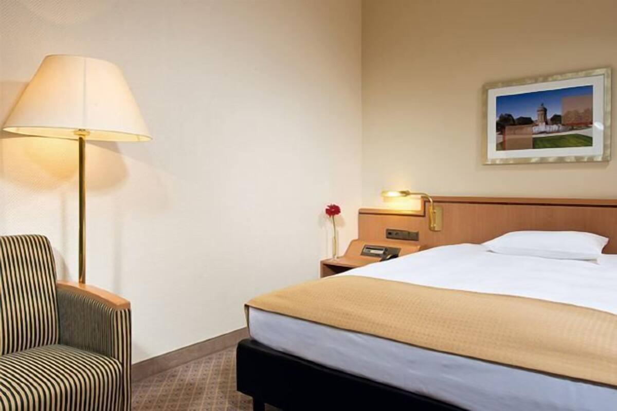 A hotel room with a bed, a chair, a lamp, a nightstand, and a picture on the wall.