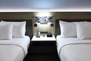 A hotel room with two beds, a nightstand with a digital clock, and a wall-mounted light fixture.