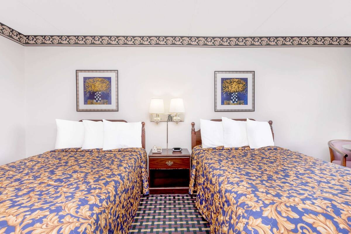 Habitación de hotel con dos camas, una mesita de noche con lámparas y dos cuadros enmarcados en la pared.