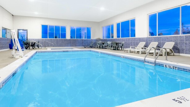 A swimming pool with clear blue water, surrounded by lounge chairs and a view of the cityscape through large windows. - Howard Johnson by Wyndham Perry GA (Perry)