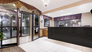 A hotel reception area with a black reception desk, glass doors leading to the lobby, and a chandelier. - Howard Johnson by Wyndham Perry GA (Perry)