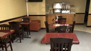 A dining area with wooden tables and chairs, a kitchen area with a coffee machine, and a sign indicating a dining hall. - Howard Johnson by Wyndham Perry GA (Perry)