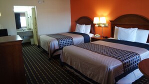 A hotel room with two beds, a nightstand with a lamp, a dresser, and a bathroom visible through an open door. - Howard Johnson by Wyndham Perry GA (Perry)