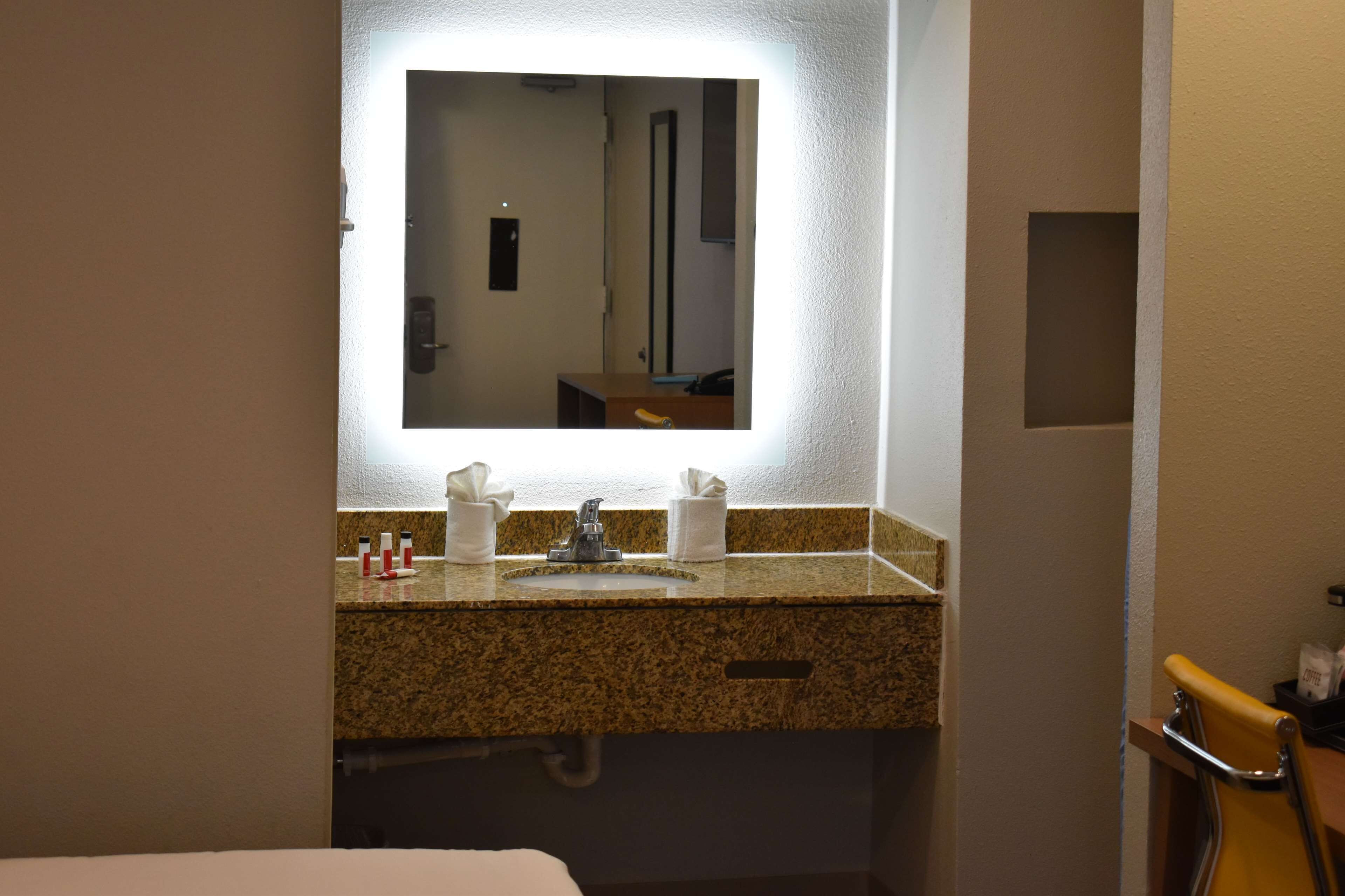 A bathroom with a granite countertop, a sink, a mirror, and a towel dispenser.