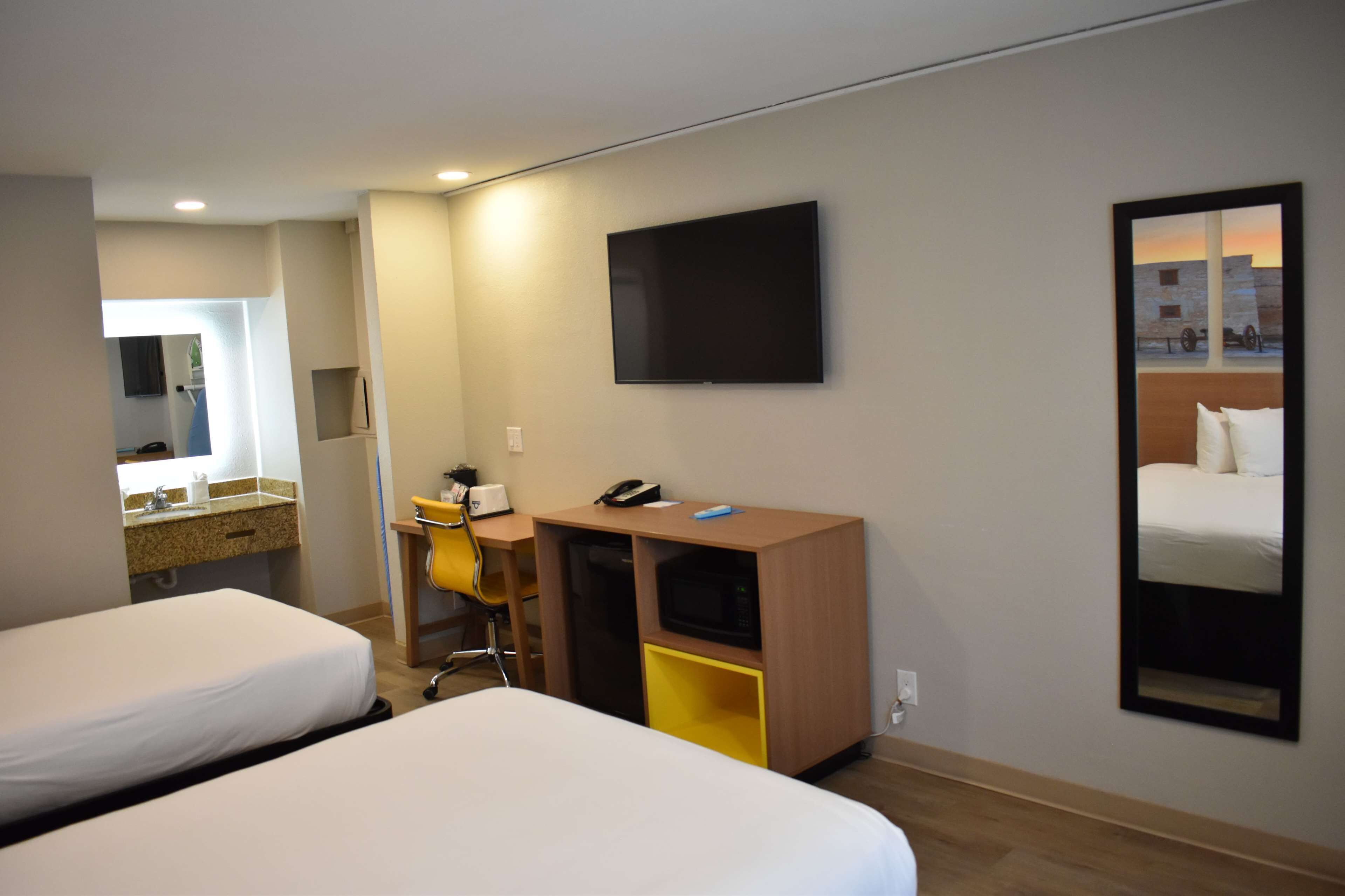 A hotel room with two beds, a desk with a chair, a microwave, and a flat-screen TV mounted on the wall.